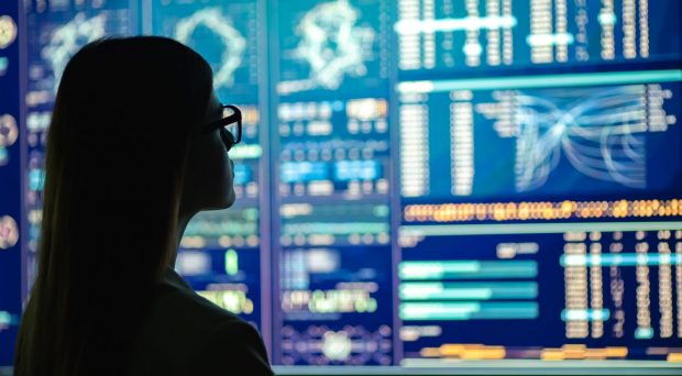 Business person looking at data dashboards displayed on screens on wall.