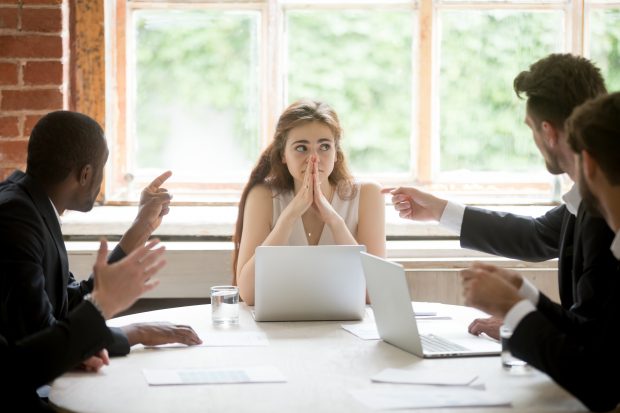 Perplexed young woman looking at coworkers pointing fingers at her. 