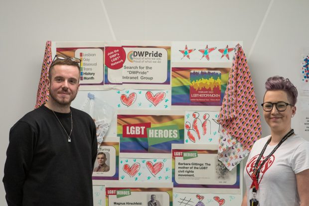 Jordan Mcnally and Amy Cross standing in front of the DWP Pride board displayed in the Manchester hub.