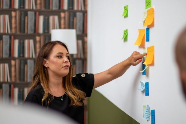 Jade Fryer, Senior Digital Performance Analyst, BPDTS pointing at post-it notes on a whiteboard.