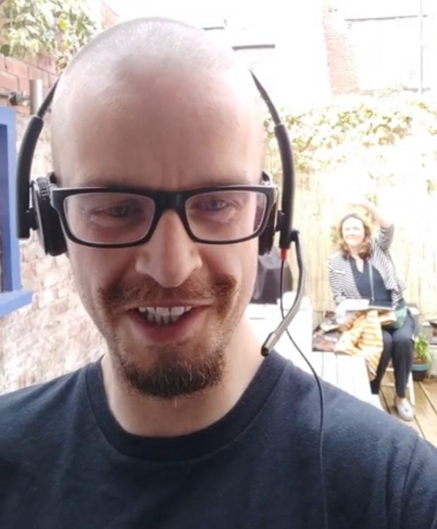 Dave Hutchinson with headphones in foreground and his wife socially distancing in background